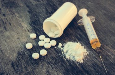drug addiction on the old wooden background. White pill, syringe and heroin. Toned image.